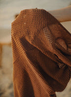 Saída Flavia, vestido curto em tricô castanho, decote gota preso por estrela do mar dourada e mangas longas. Chic, semi-transparente e perfeita para resorts.
