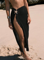 Saia de praia Étoile Ellie, tecido plissado semi-transparente, fenda lateral profunda e estrela do mar dourada. Preto e cáqui para um look resort luxuoso.