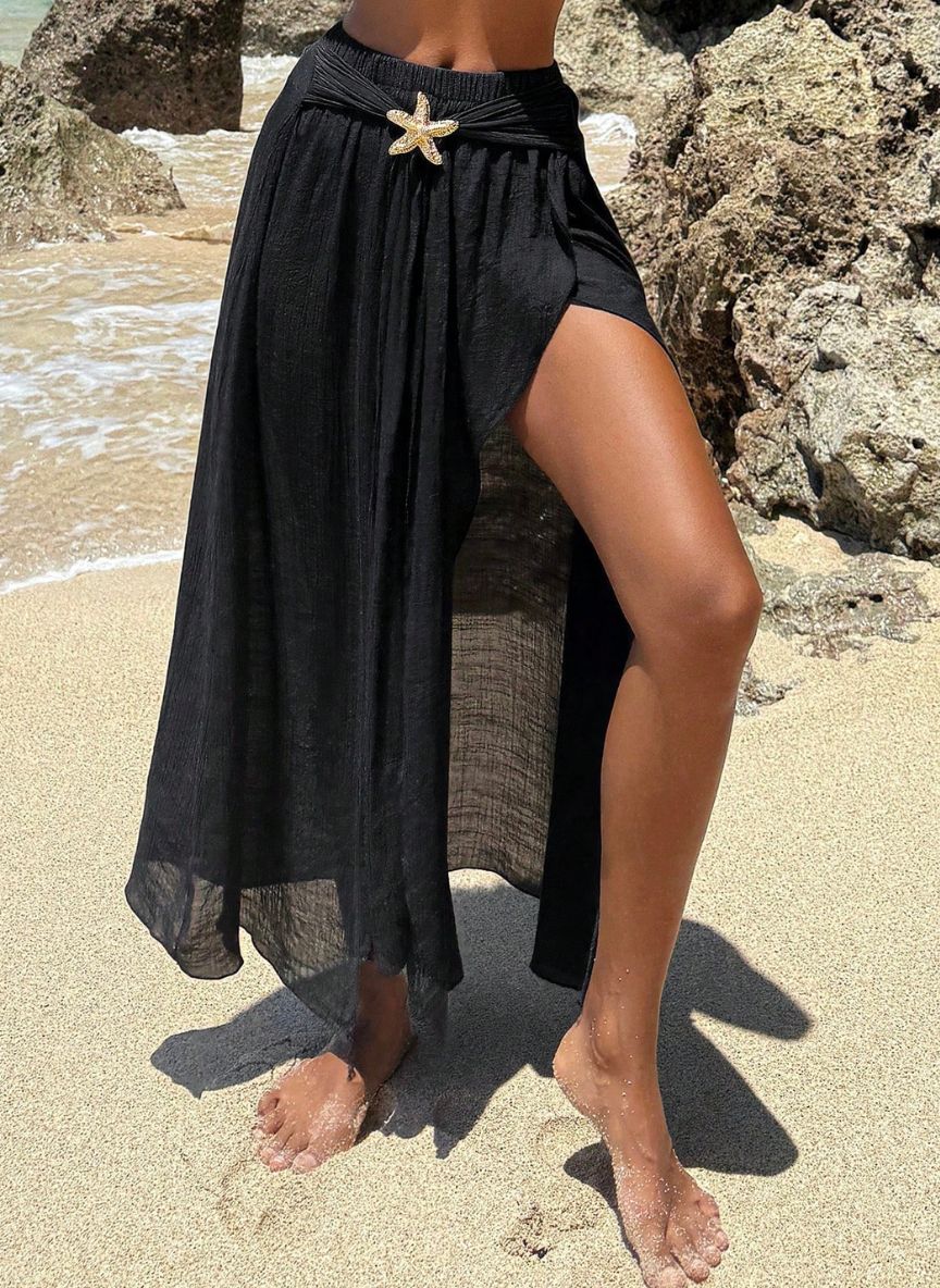 Saída de Praia Lucie, tecido viscose preto, fenda lateral sensual, estrela do mar dourada e nó divisor. O luxo boho para transitar da praia ao resort com elegância.